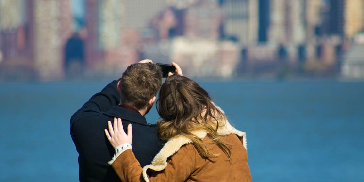 Couple taking photo of city skyline across a body of water