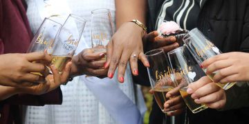 Women holding drinking glasses and looking at a ring on someone's hand