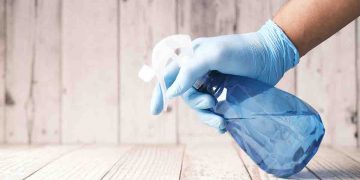 Person with gloves and spray bottle cleaning.