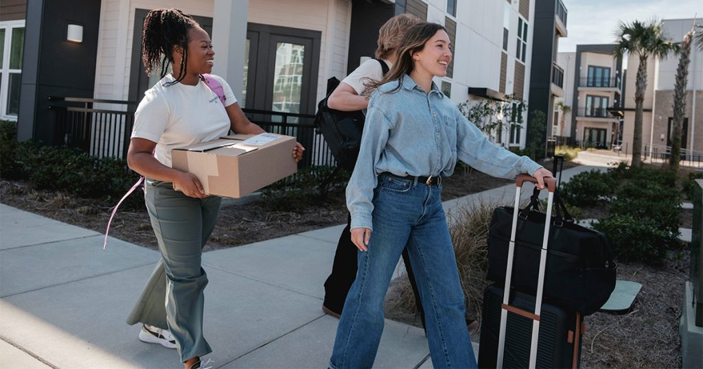 Group of young people moving and carrying boxes and suitcases down a sidewalk. 