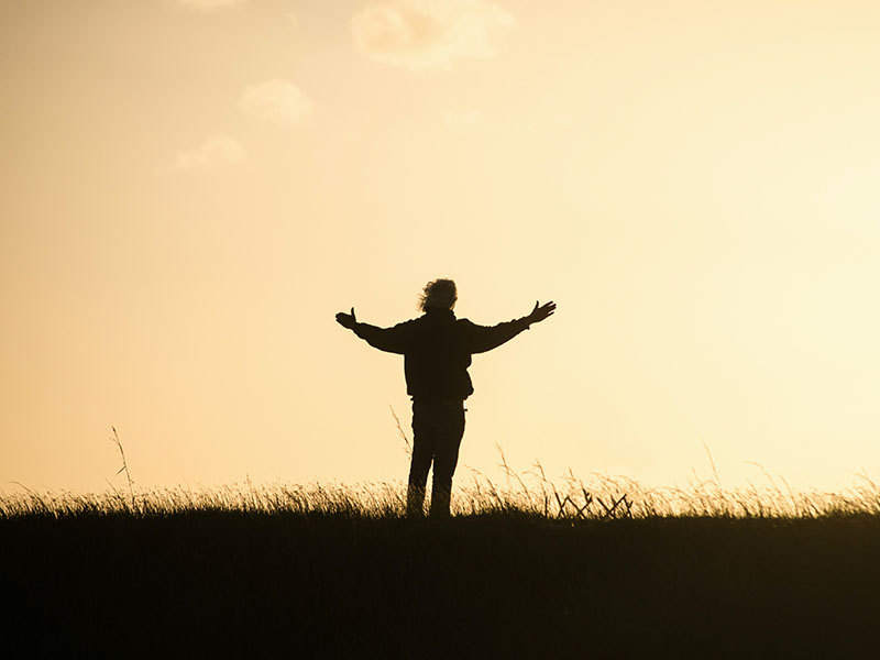 Person standing with arms open during sunset