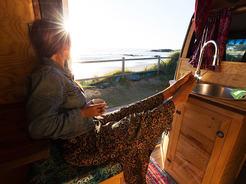 Young woman in camper van at sunrise by the beach